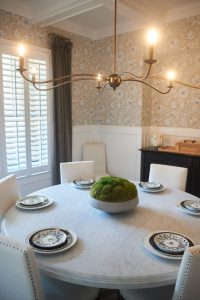 Dining room with floral wallpaper, round marble table and moss centerpiece