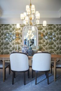 Green botanical wallpapered dining room with white chairs and chandelier