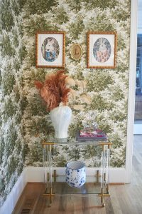 Green botanical wallpaper with framed art above a console and stools