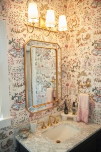 Powder room with pink floral wallpaper, gold mirror and sconces