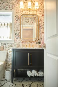 Powder room with floral wallpaper, black vanity, gold mirror and hexagon tile floor