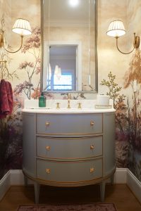 Powder room with floral wallpaper, blue-green vanity and gold mirror