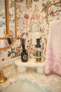 Powder room with floral wallpaper, marble vanity and gold mirror