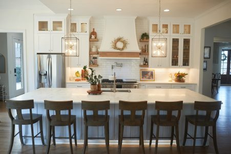 White kitchen with large island, bar stools and stainless refrigerator