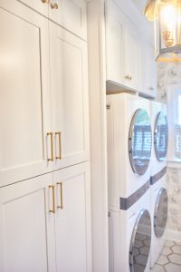 White laundry room cabinetry with brass hardware and stacked washer and dryer